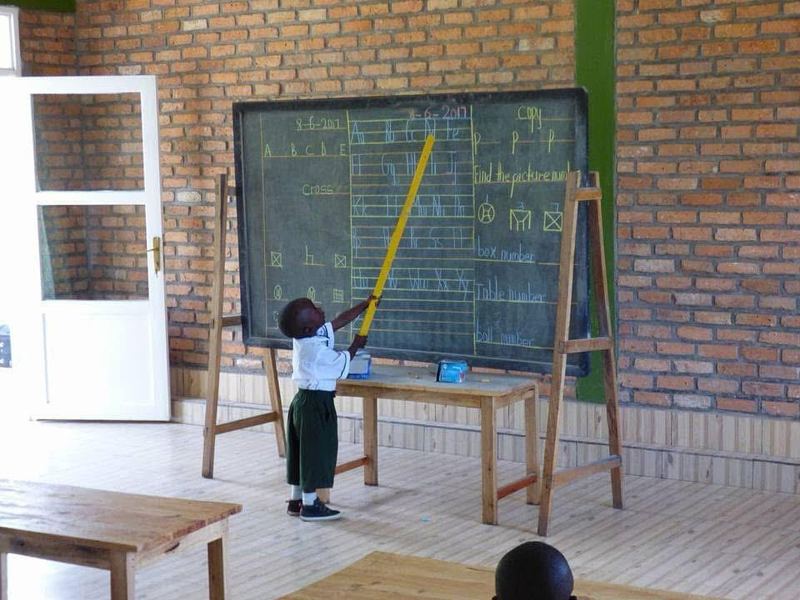 A young pupil pointing at the blackboard with a long yellow pointer in a brick classroom