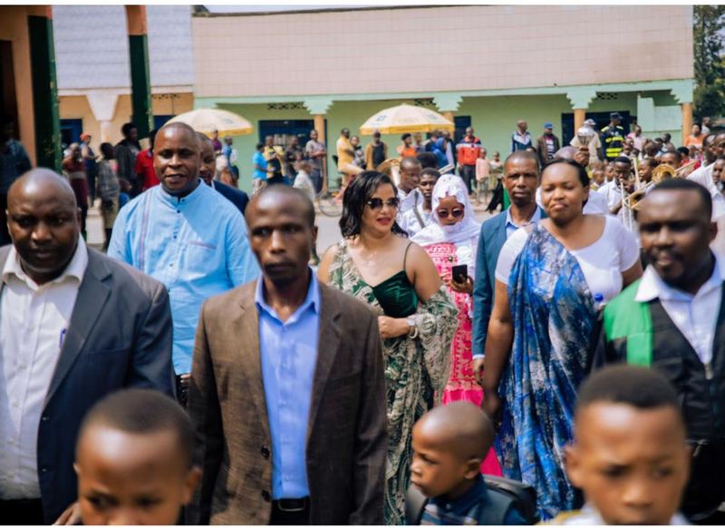 Adults and children in a crowd in front of a building, umbrellas behind them