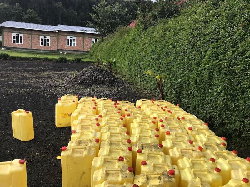 Rows of yellow jerrycans on dark ground in front of a school building
