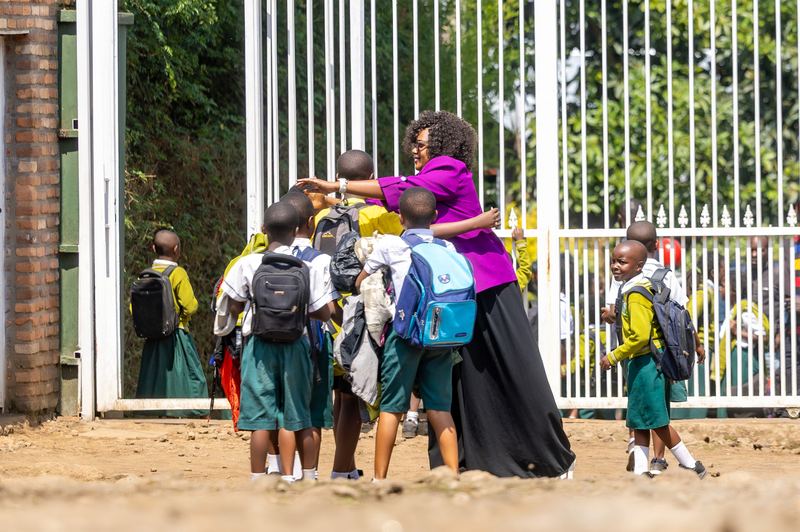 Faith Uwantege in a purple jacket and long black skirt hugging pupils with school bags at the school gate