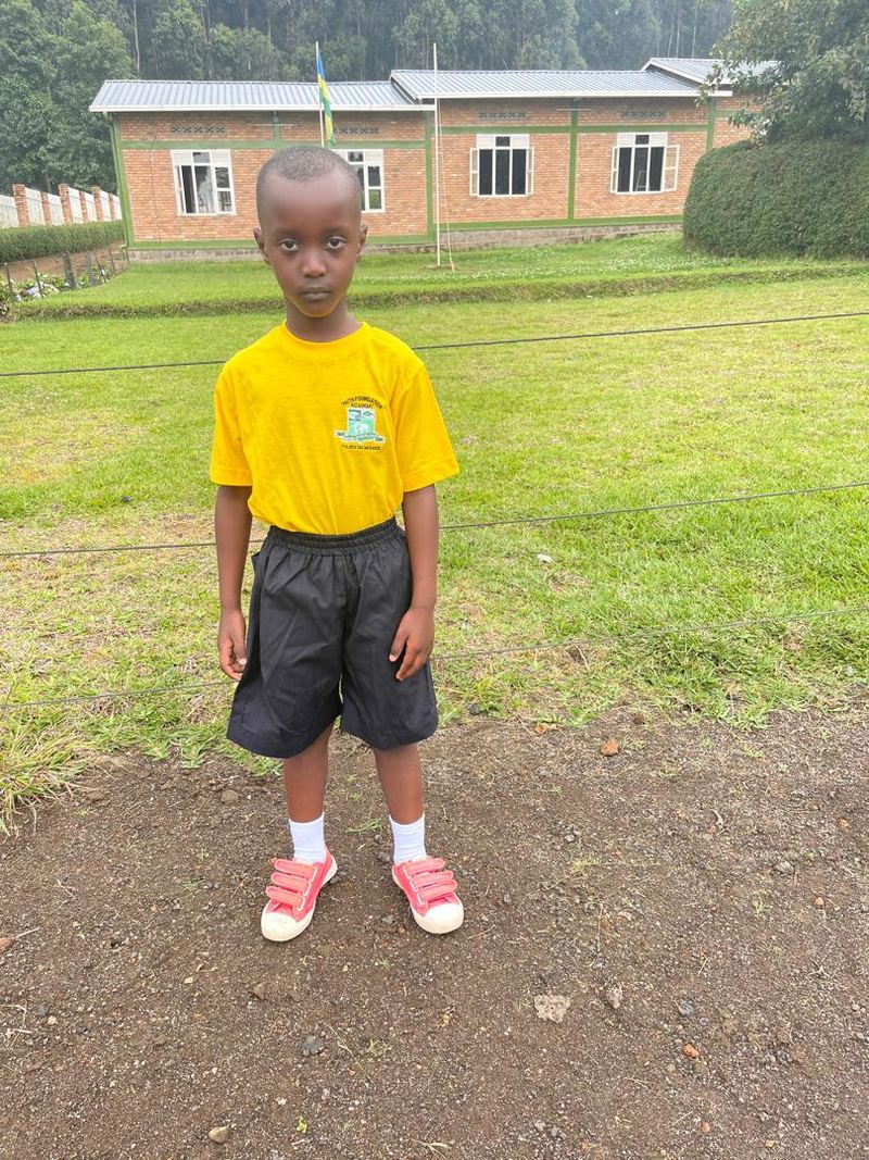 A young pupil in a yellow school T-shirt and black shorts standing on the school grounds