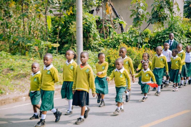 Young pupils in yellow jumpers and green uniform walking along a road in a long line