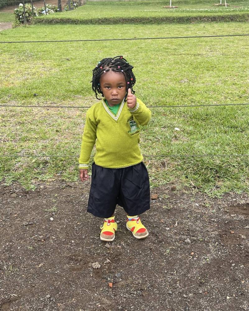 A young girl in a green school jumper giving a thumbs up on the school grounds