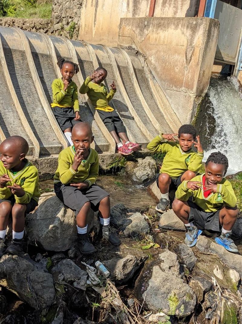 Pupils in yellow jumpers sitting on rocks beside a concrete water channel